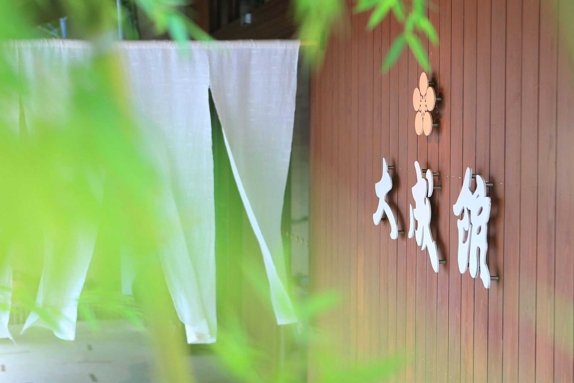 Gensen Yuyado Taiseikan (TAISEIKAN) with white entrance noren hanging among fresh bamboo leaves.