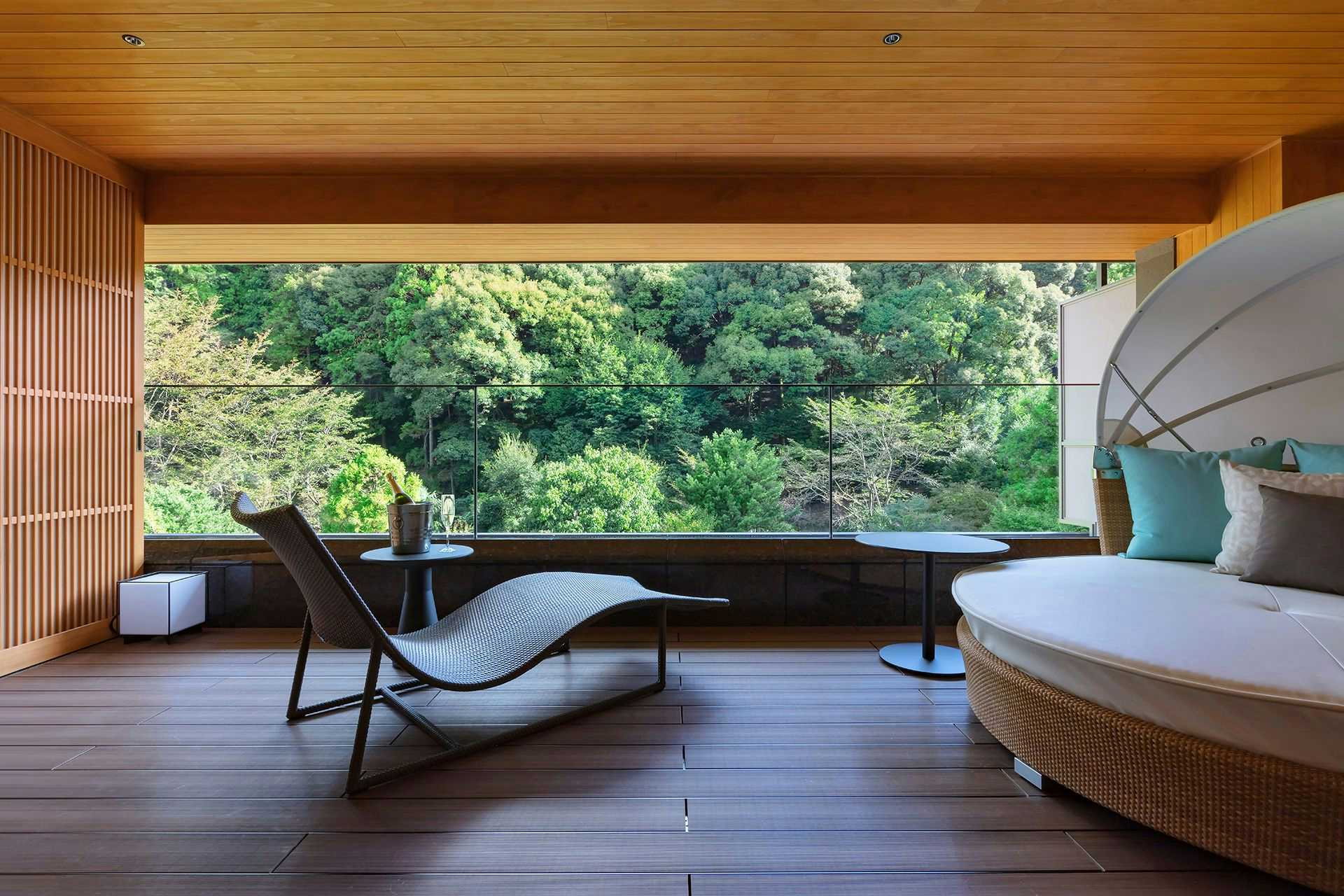 Otanisanso with this scene, where a window-lined guest room places a curved chaise beside a bed and forest view.