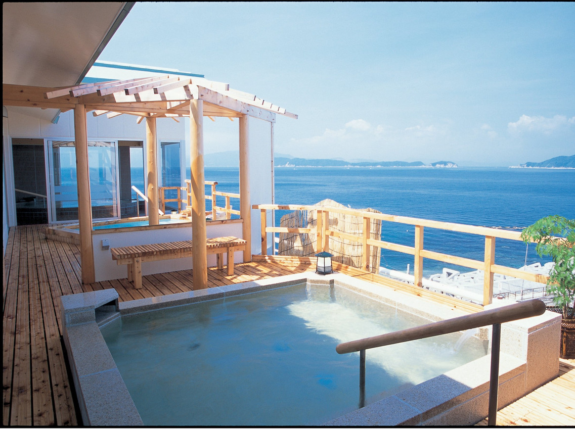 An outdoor rectangular bath on a timber terrace overlooking blue water.