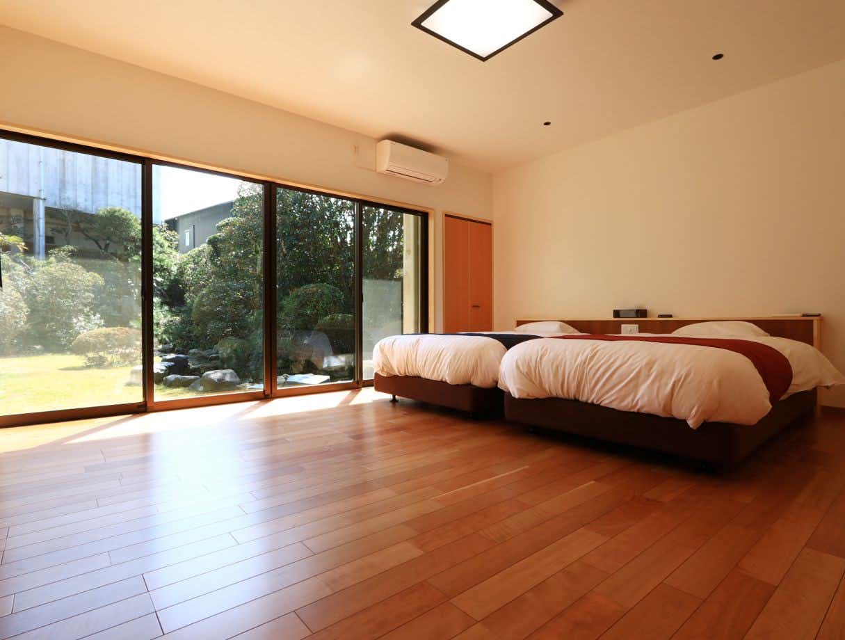 Masuya Ryokan a spacious twin bedroom with seating beside garden windows.