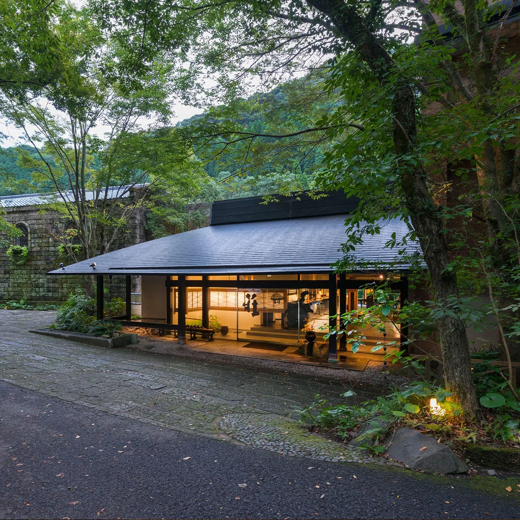 Myoken Ishiharaso's lantern-lit entrance pavilion glowing at dusk beneath forest trees