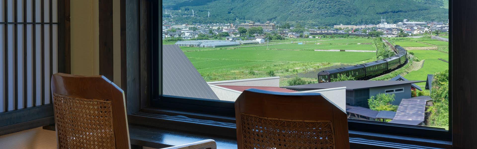 Yufuin Onsen Higashi Shouan with two wicker chairs overlooking rice fields and distant hills.