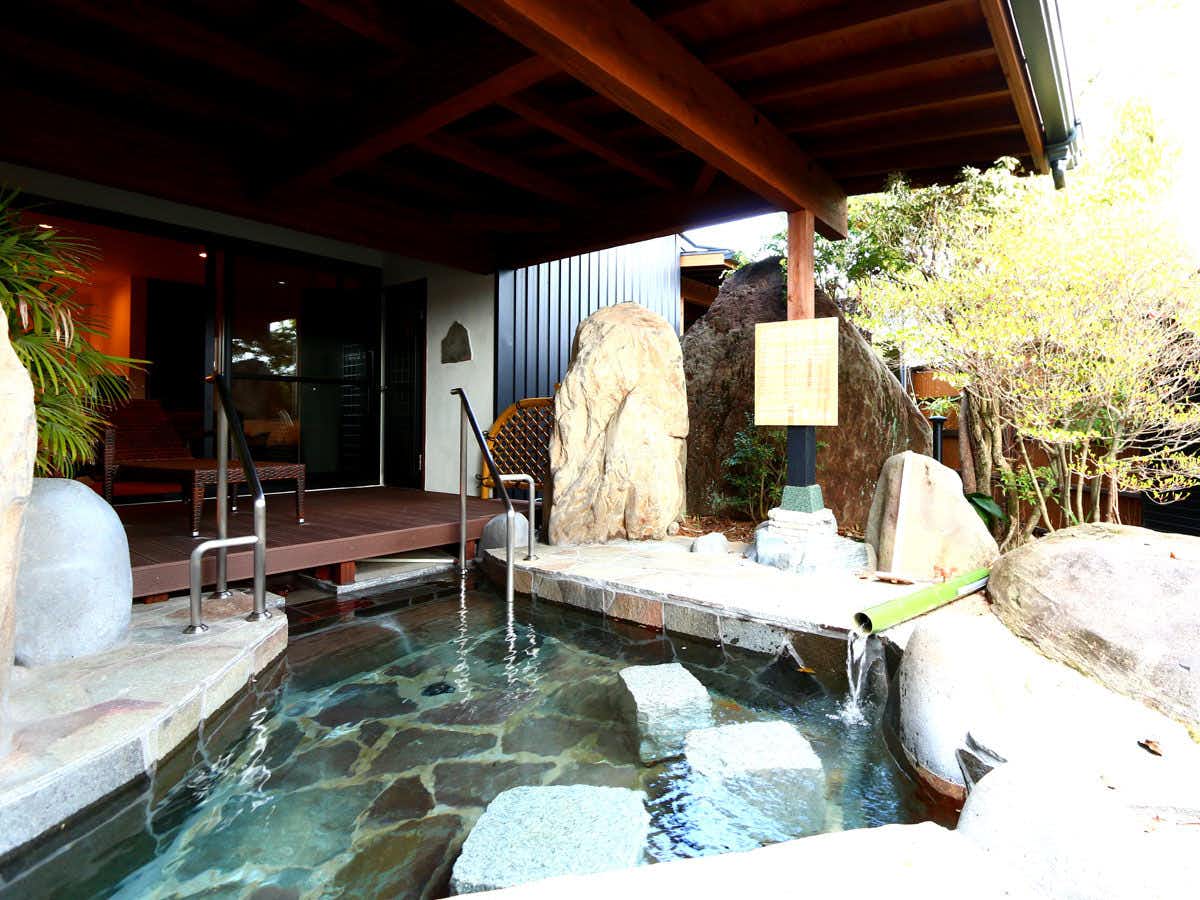 Hirayama Onsen Uedaya rock-lined bath beneath a roof beside garden stones and foliage