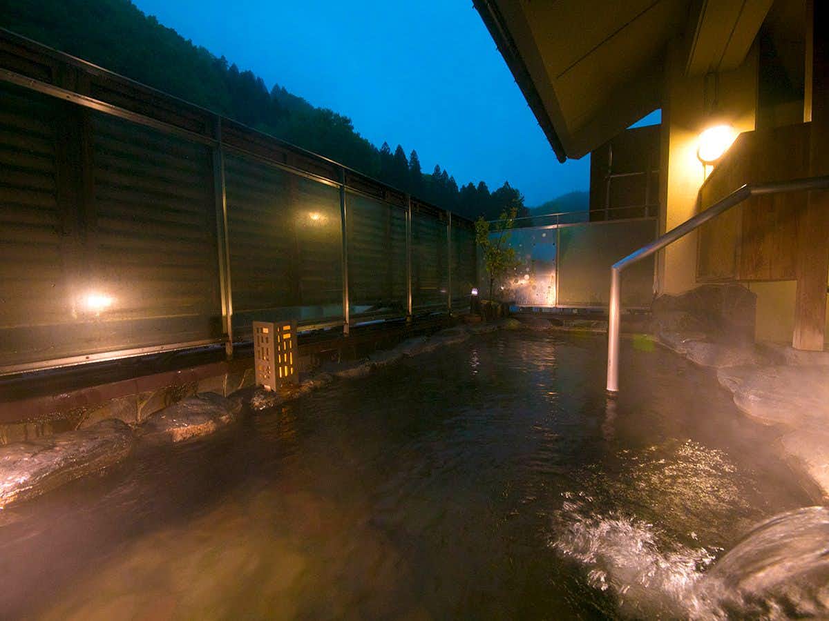Tsuchiyu Onsen Gensen Yuan New Ougiya with an outdoor rock bath surrounded by fresh green foliage.