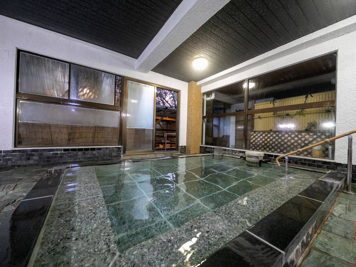A covered bath is surrounded by dark stone and windows.