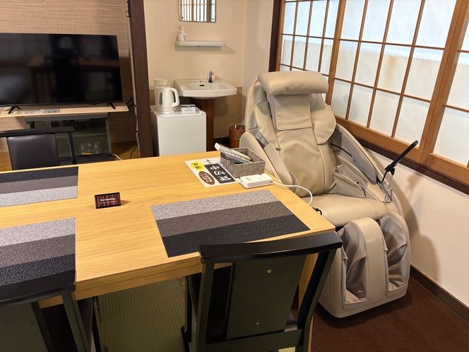 A guest room with a table, television, and massage chair.