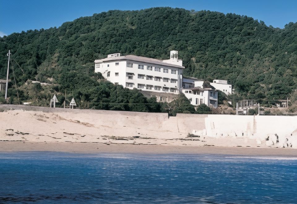 A white lodging building on a wooded slope above the sea.