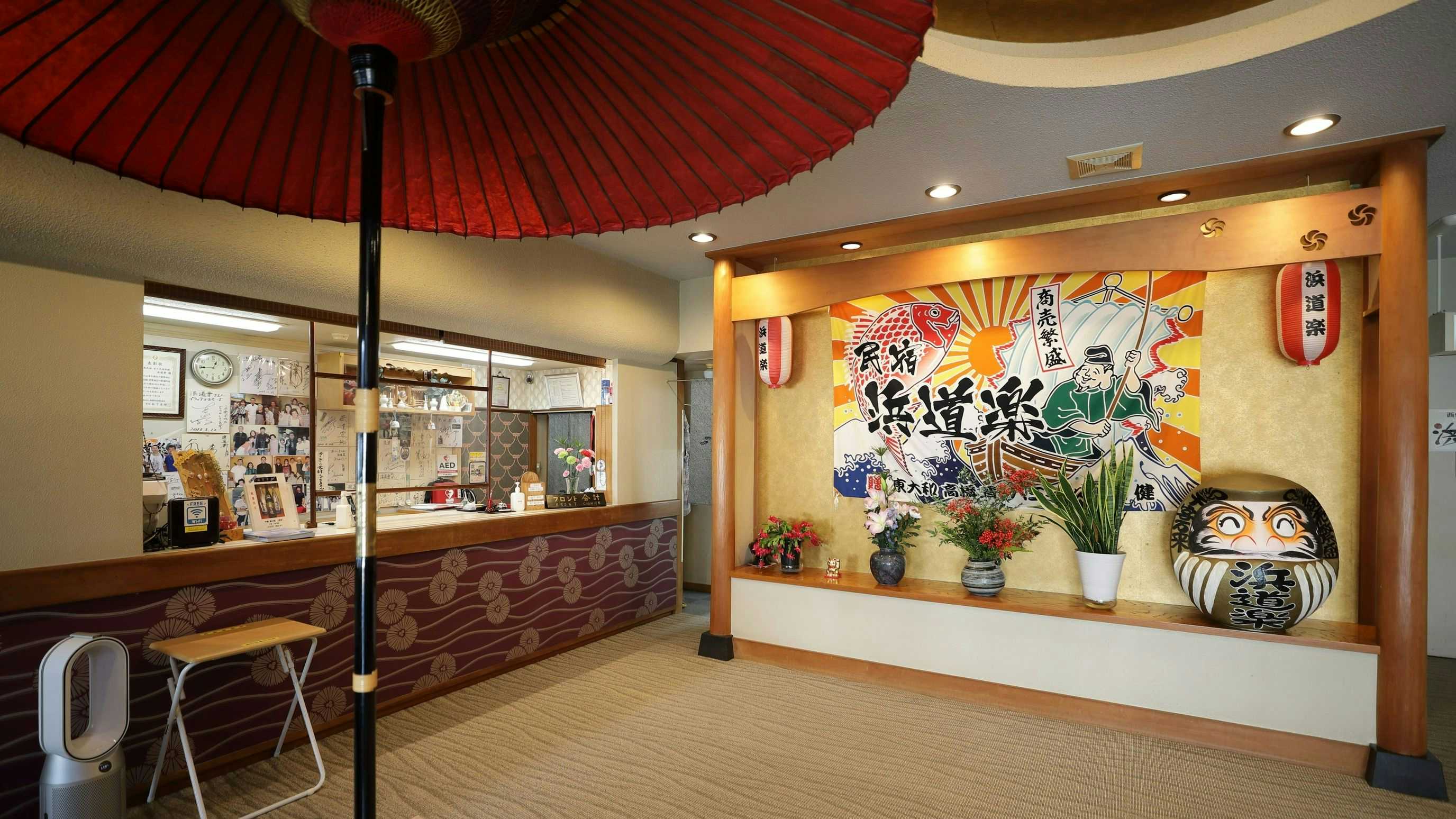 Kumomi Onsen Hamadoraku with a colorful lobby displaying parasols, flowers, and daruma figures.