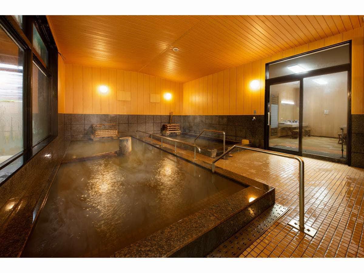 Sugatani Onsen Large indoor bath with tiled floor, metal handrails, warm wooden walls, washing area, and adjoining doorway