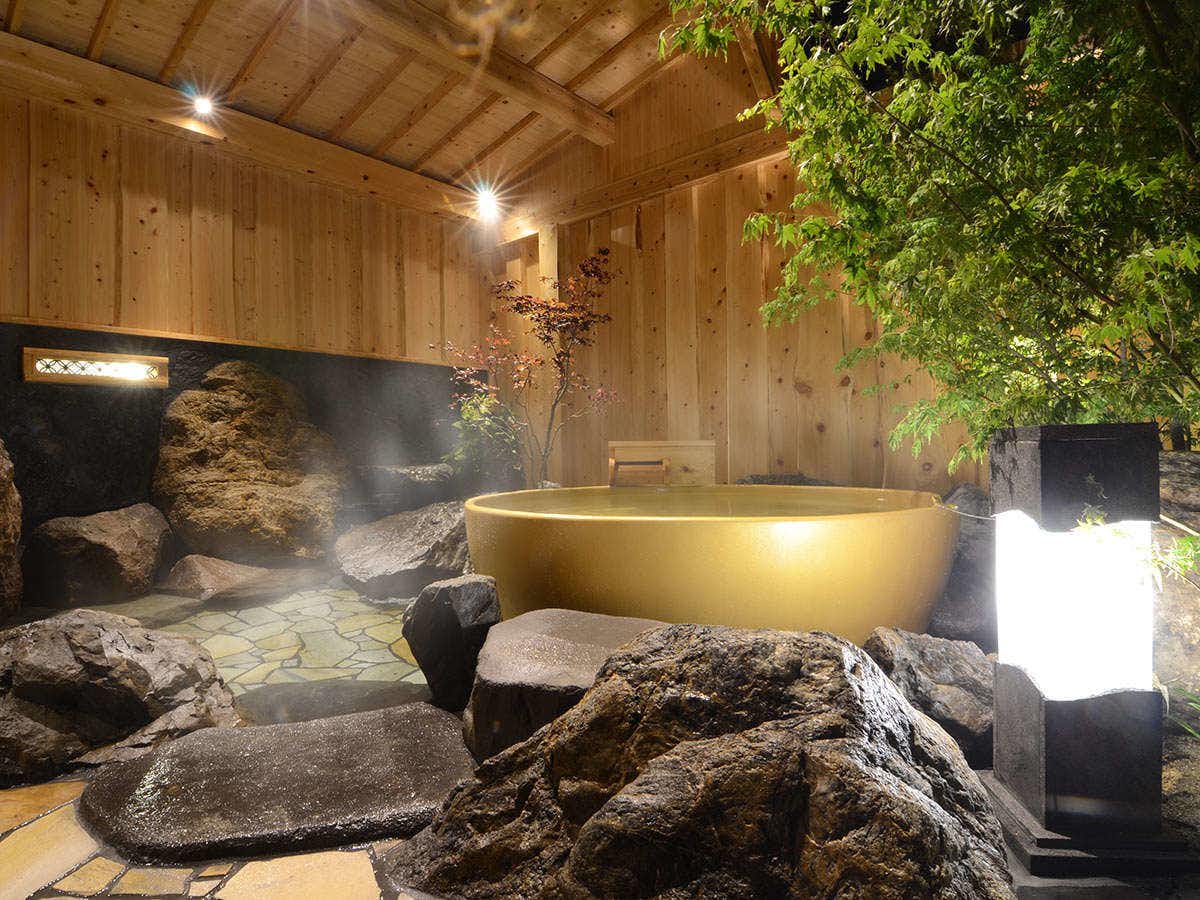 Japanese Inn Utsuwa Beppu Kannawa with a round outdoor bath surrounded by rocks and timber walls.