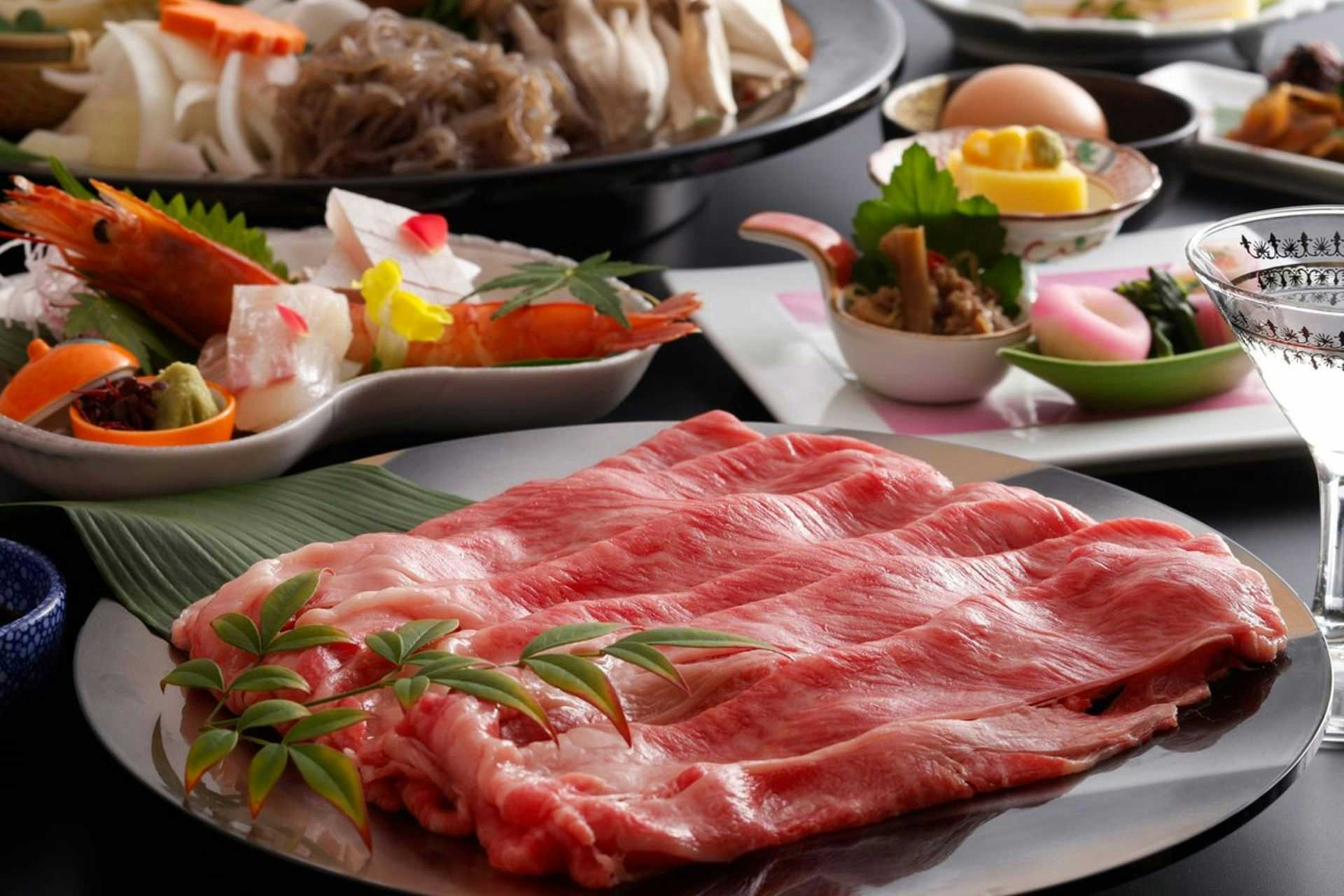 Kinosaki Ryokufukaku Sliced meat on white ceramic plate with green herb leaf and yellow citrus garnish, accompanied by small white and black serving bowls