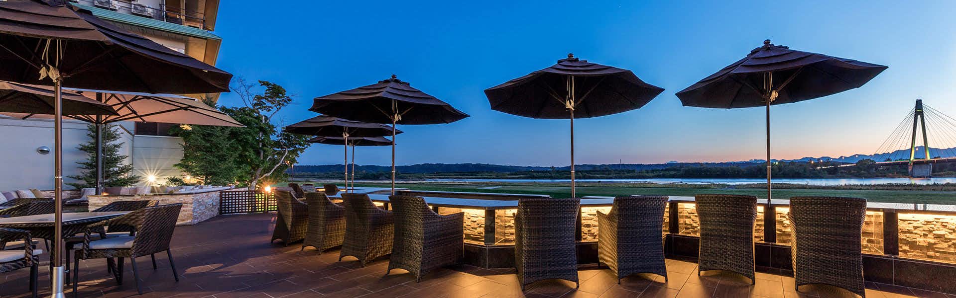 Tokachigawa Onsen Daiichi Hotel with a waterside terrace with tables, chairs, and black parasols.