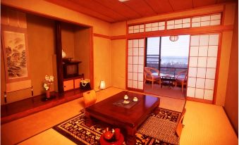 A tatami guest room with a low table and coastal town view.