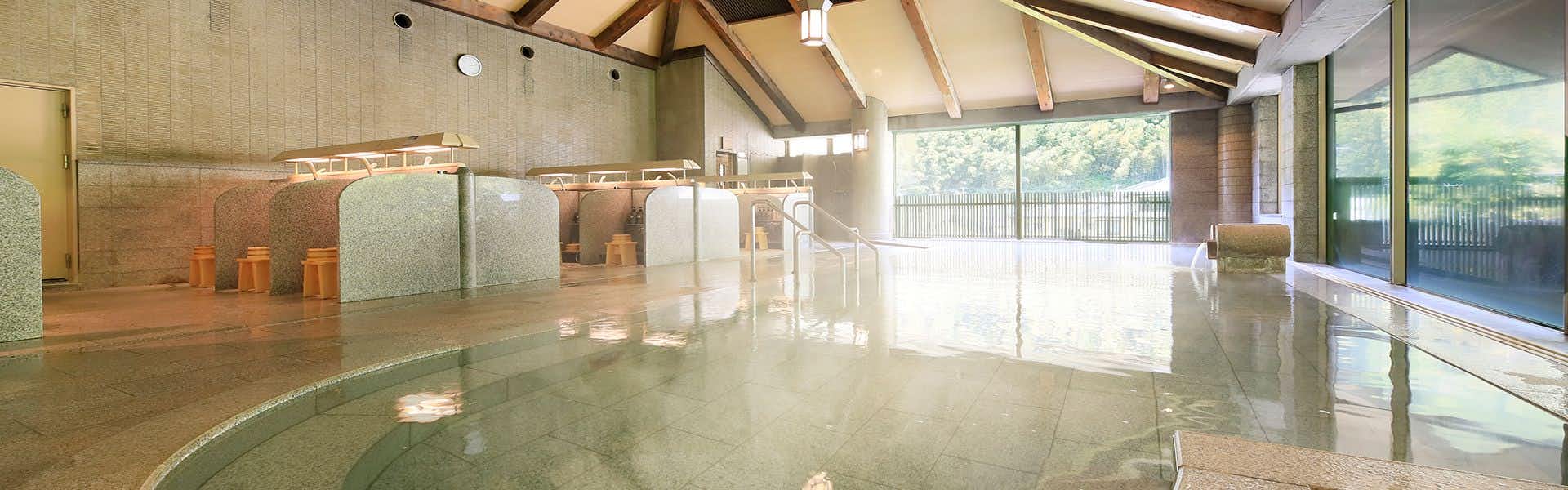 Bankokuya Large indoor bath with reflective water surface, exposed wooden ceiling beams, and natural light from windows.