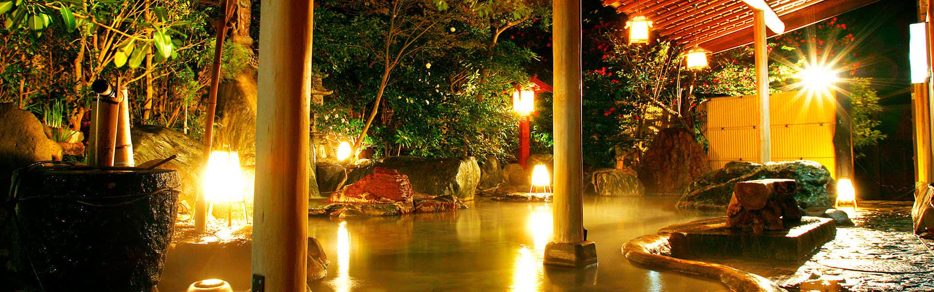 Bokusuisou Toikan Nighttime exterior showing illuminated bath with wooden deck, lanterns, stone features, and surrounding foliage.