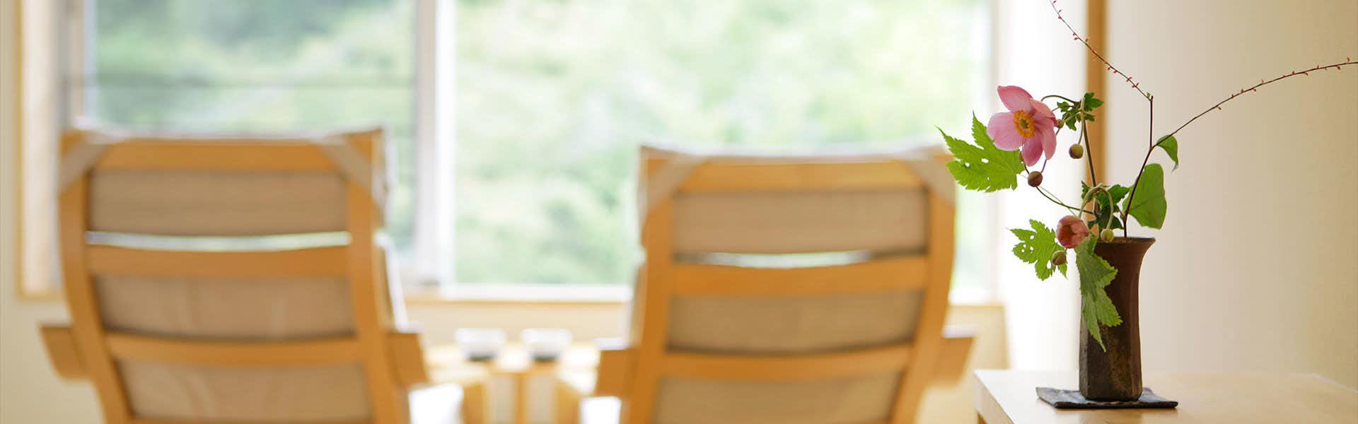 Kusatsu Hotel Annex Wata no Yu Wooden chairs with horizontal slat backs, white flowers in brown ceramic vase, window with landscape view.