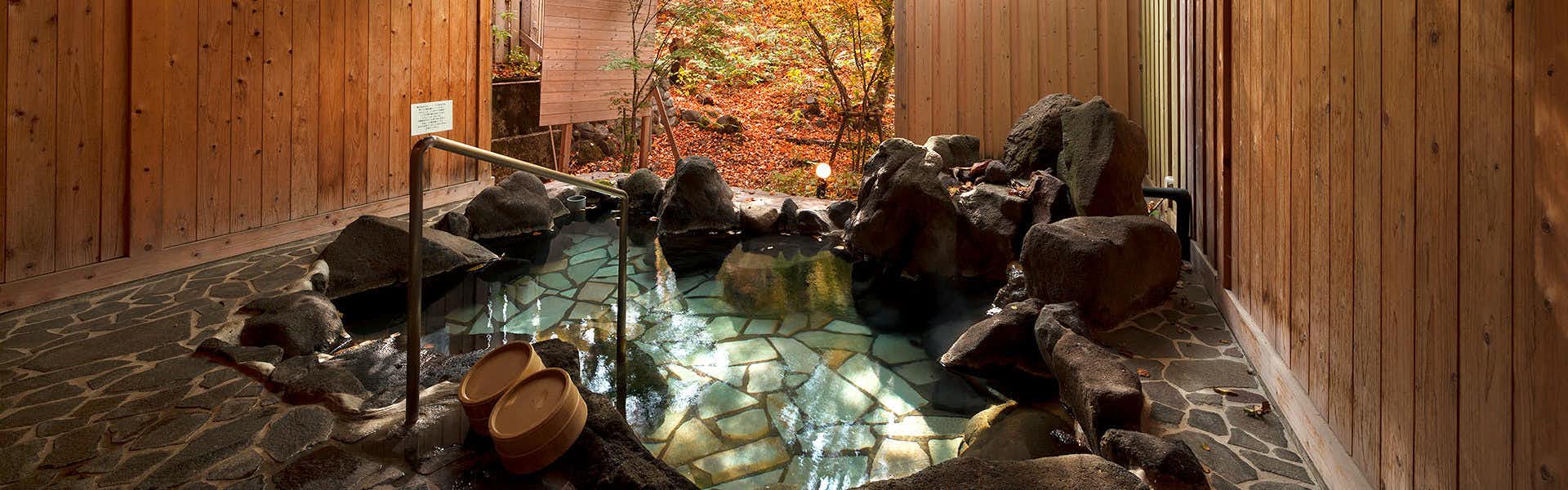 Yama no Tabisha Nakaodaira rock-lined bath with wood walls beneath red-leaved trees
