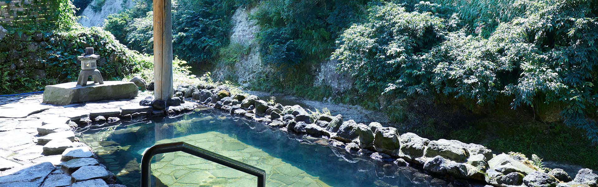 Furusato Inn of Four Seasons Colors with an outdoor rock bath surrounded by dense green woodland.