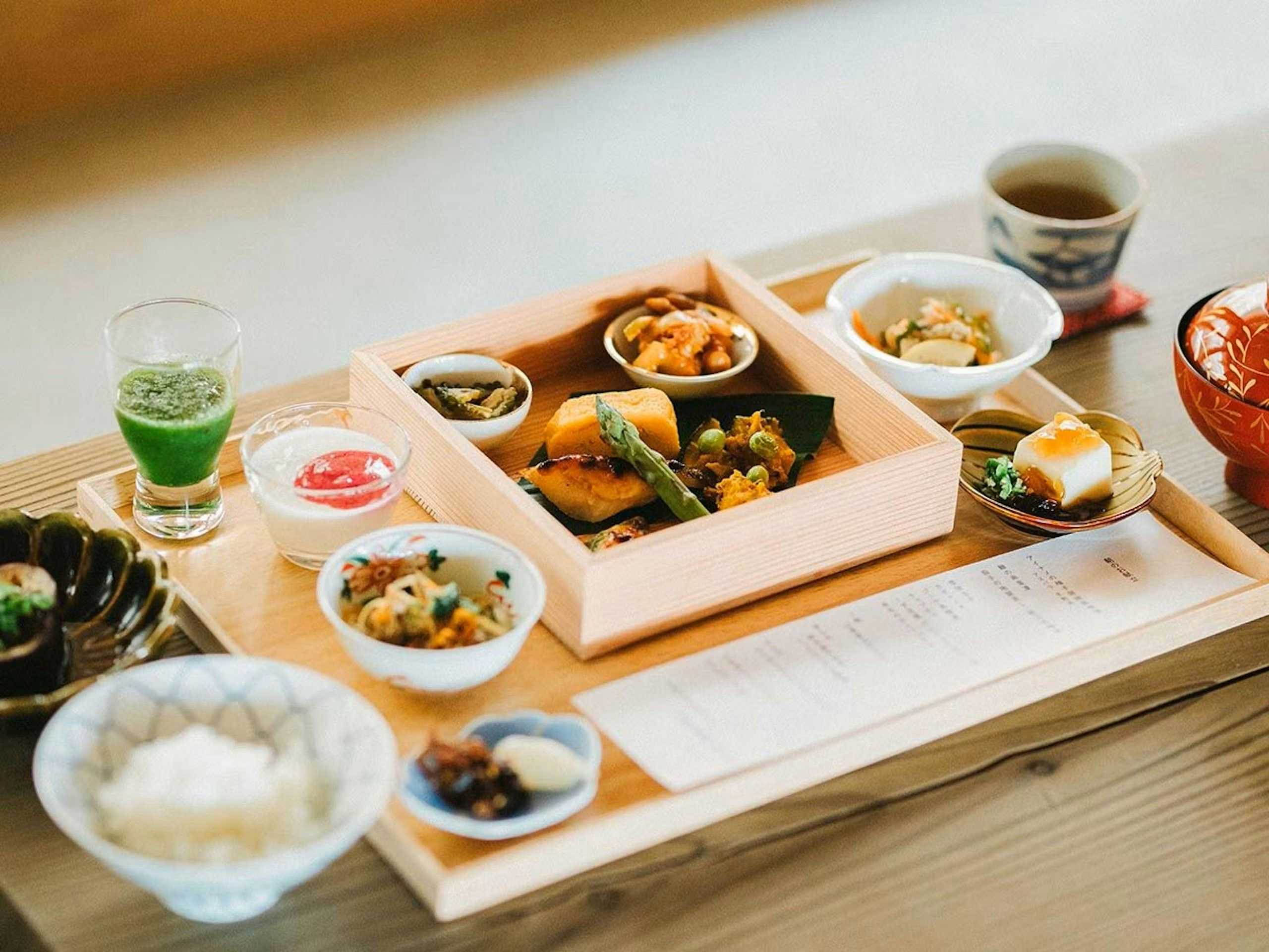 Nisaino Yuyado Asahiya Wooden tray set with many small bowls, dishes, glasses, cup, and covered vessel arranged across a pale tabletop