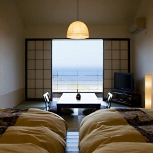 A Small Inn with Natural Hot Spring Flow: Ayu no Kaze Guest room with two white futon beds, low table, floor chairs, television, shoji screens, and a broad ocean view