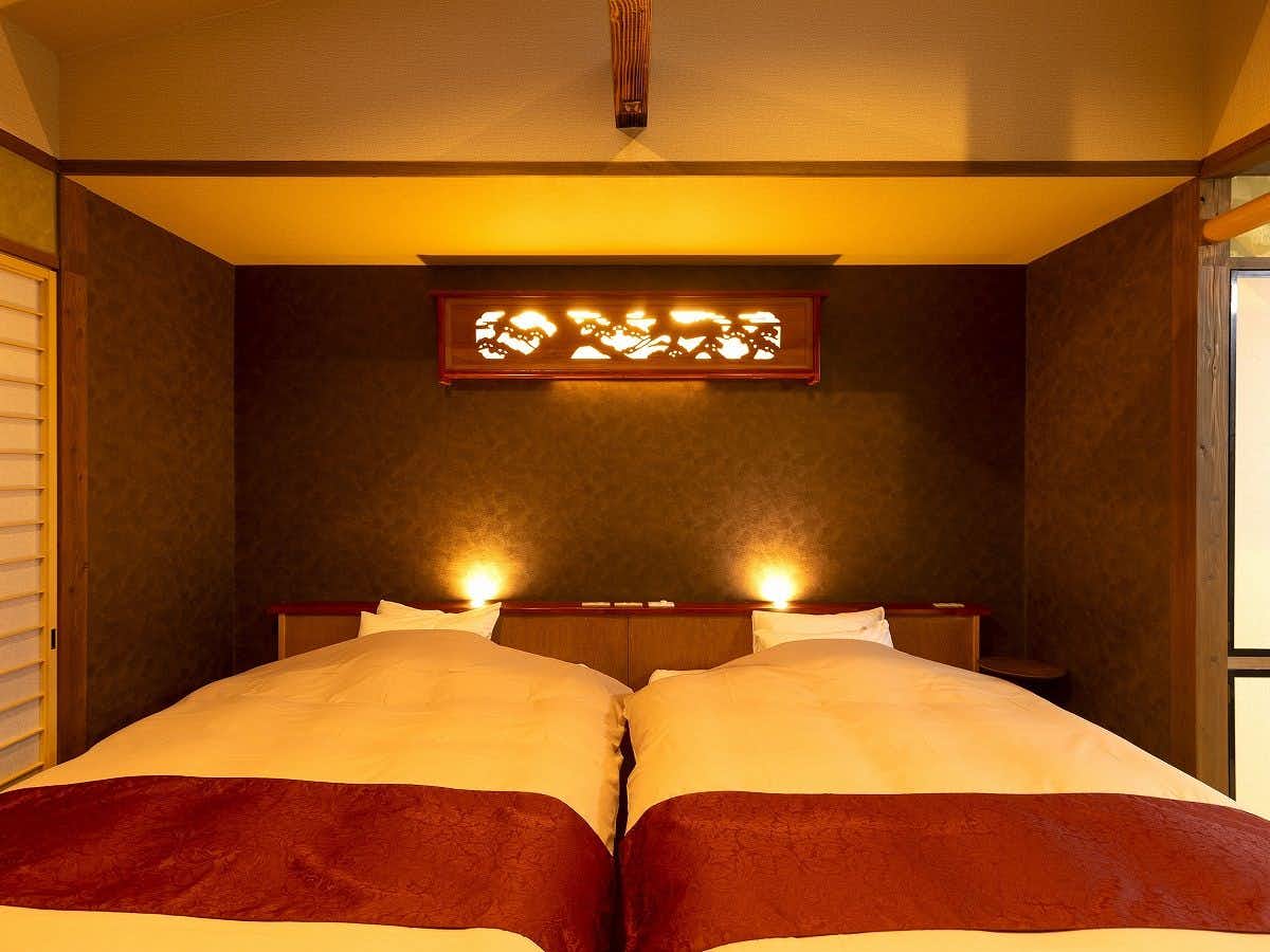 Onyado Yufuin-tei with a twin bedroom with dark headboard and red runners.