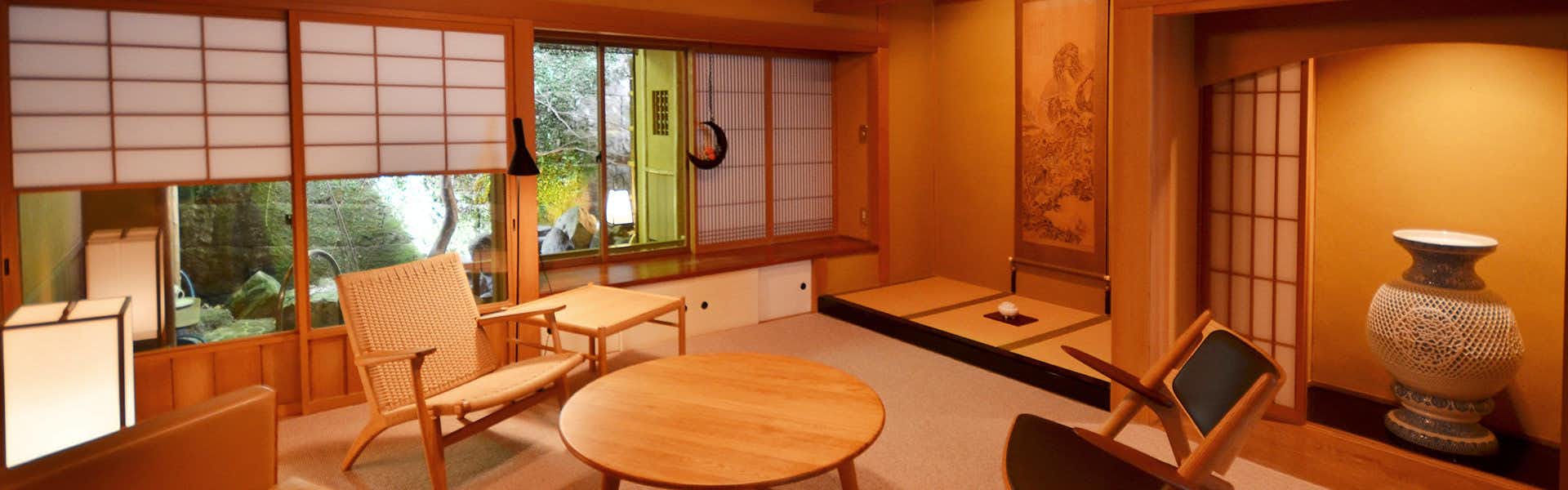 Kaiseki Inn Ogiya Wooden chair with geometric frame, round table, and warm ambient lighting in room with large windows showing greenery.
