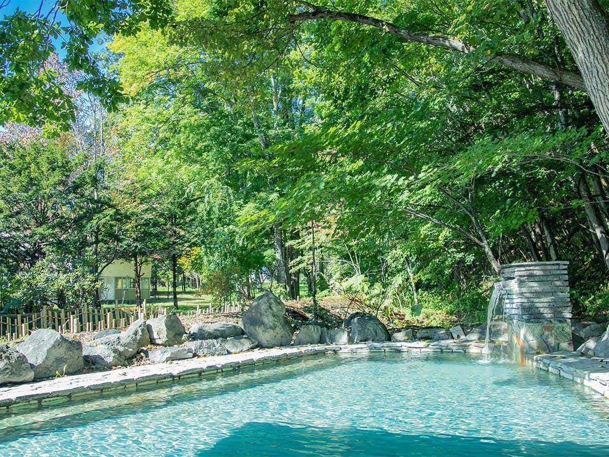 Ryokan Shiobetsu Tsurutsuru Onsen with a turquoise outdoor bath shaded by mature green trees.