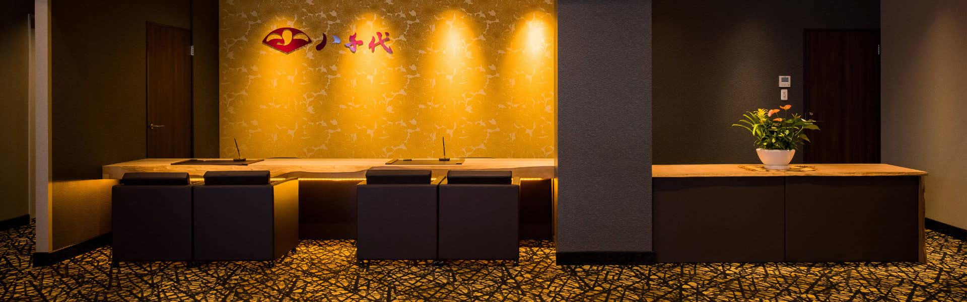Dogo Onsen Yachiyo with the warmly lit reception desk beside a flower arrangement.