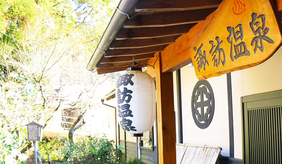 Inn entrance beneath a wooden Suwa Onsen sign and hanging lantern.