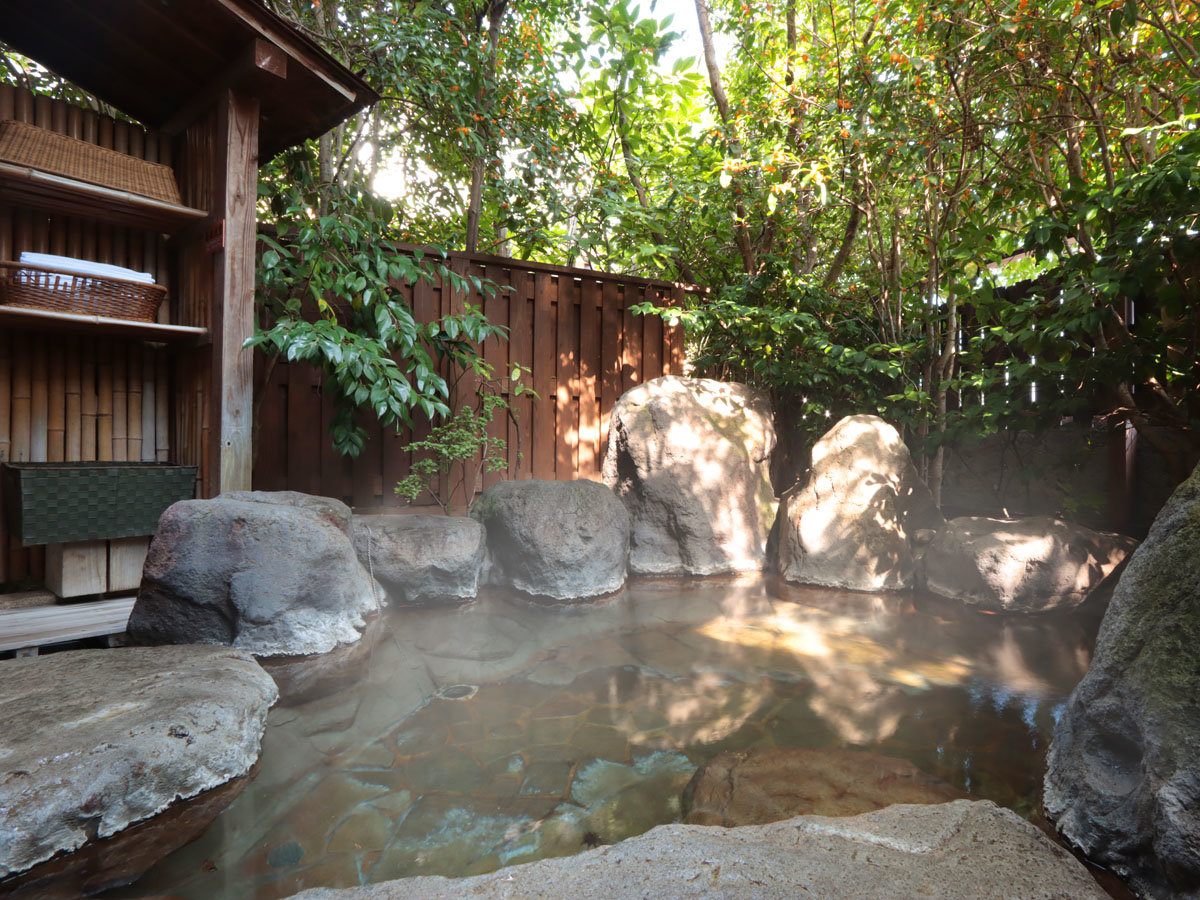 A rock-lined outdoor bath sits within a secluded leafy courtyard.