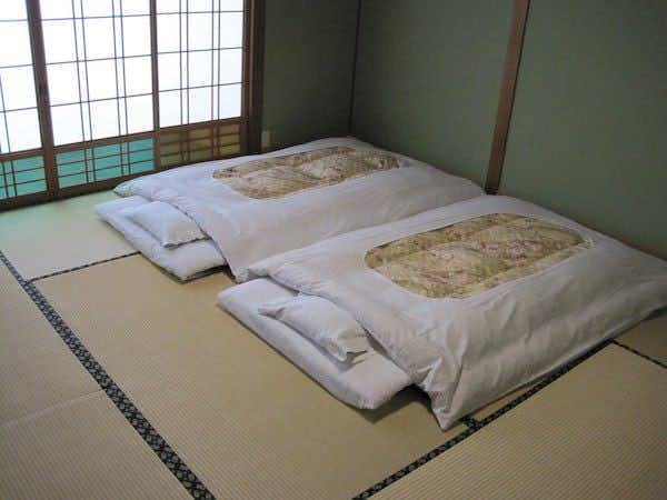 Suminoe Ryokan Tatami room with two white beddings with patterned covers arranged on floor, green walls, and shoji screen window.