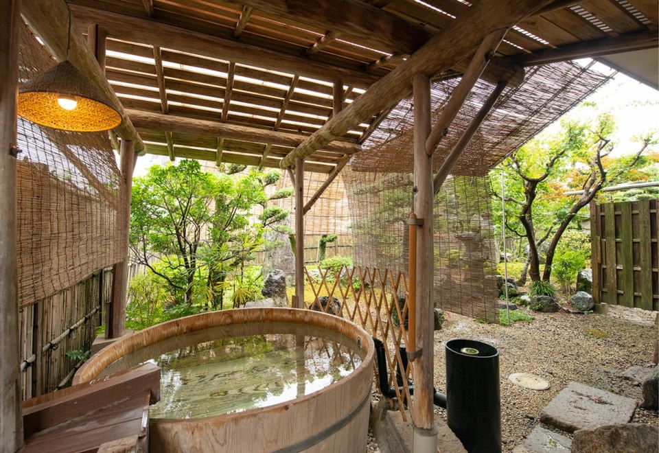 Private outdoor soaking tub under a covered garden shelter.