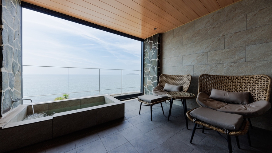 A sea-view bathing terrace with a rectangular tub and woven lounge chairs.