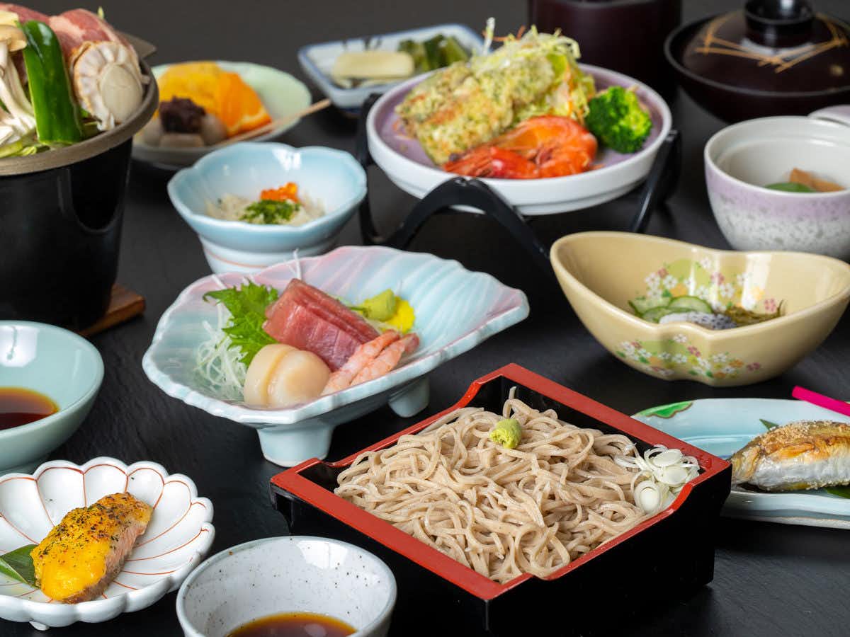 Shima Onsen Kotobukiya Ryokan multiple bowls and plates of prepared items: colored vessels containing greens and food, red dish with preparations, yellow and orange items.