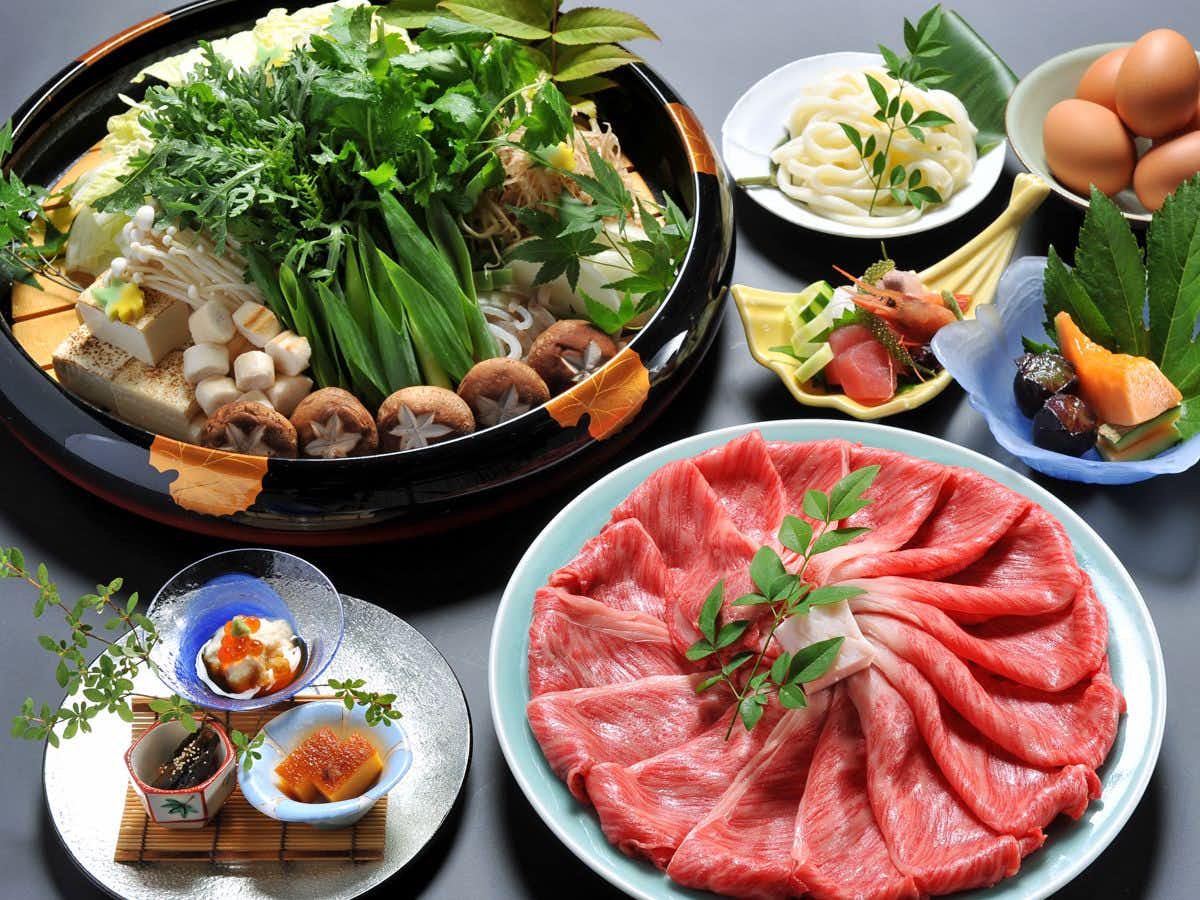 Watazen Ryokan with thinly sliced beef presented with leafy vegetables and small dishes.