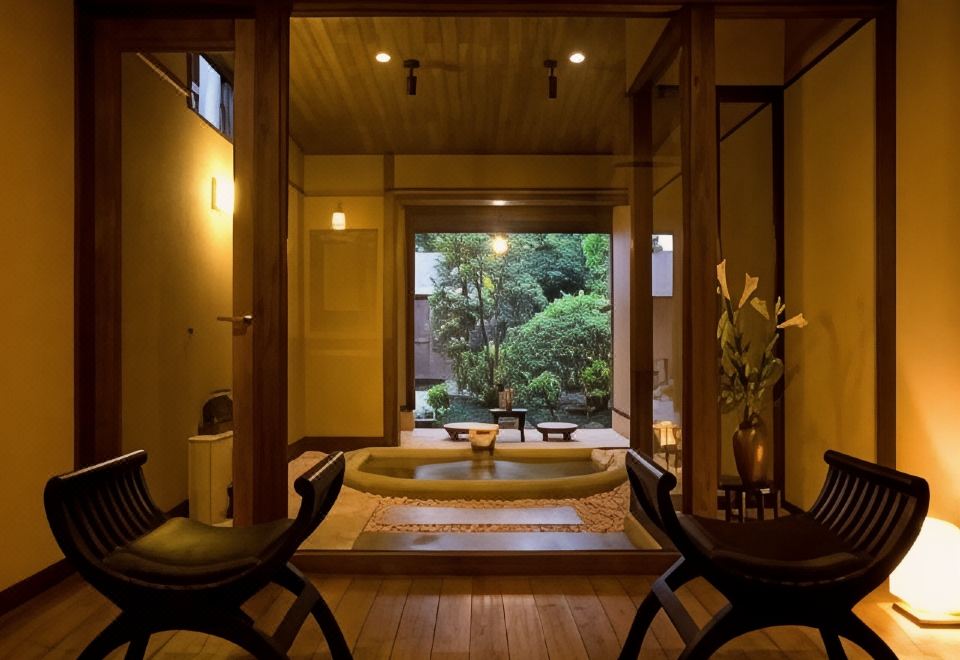 Private indoor bathing area with a square tub, lounge chairs and a garden view.
