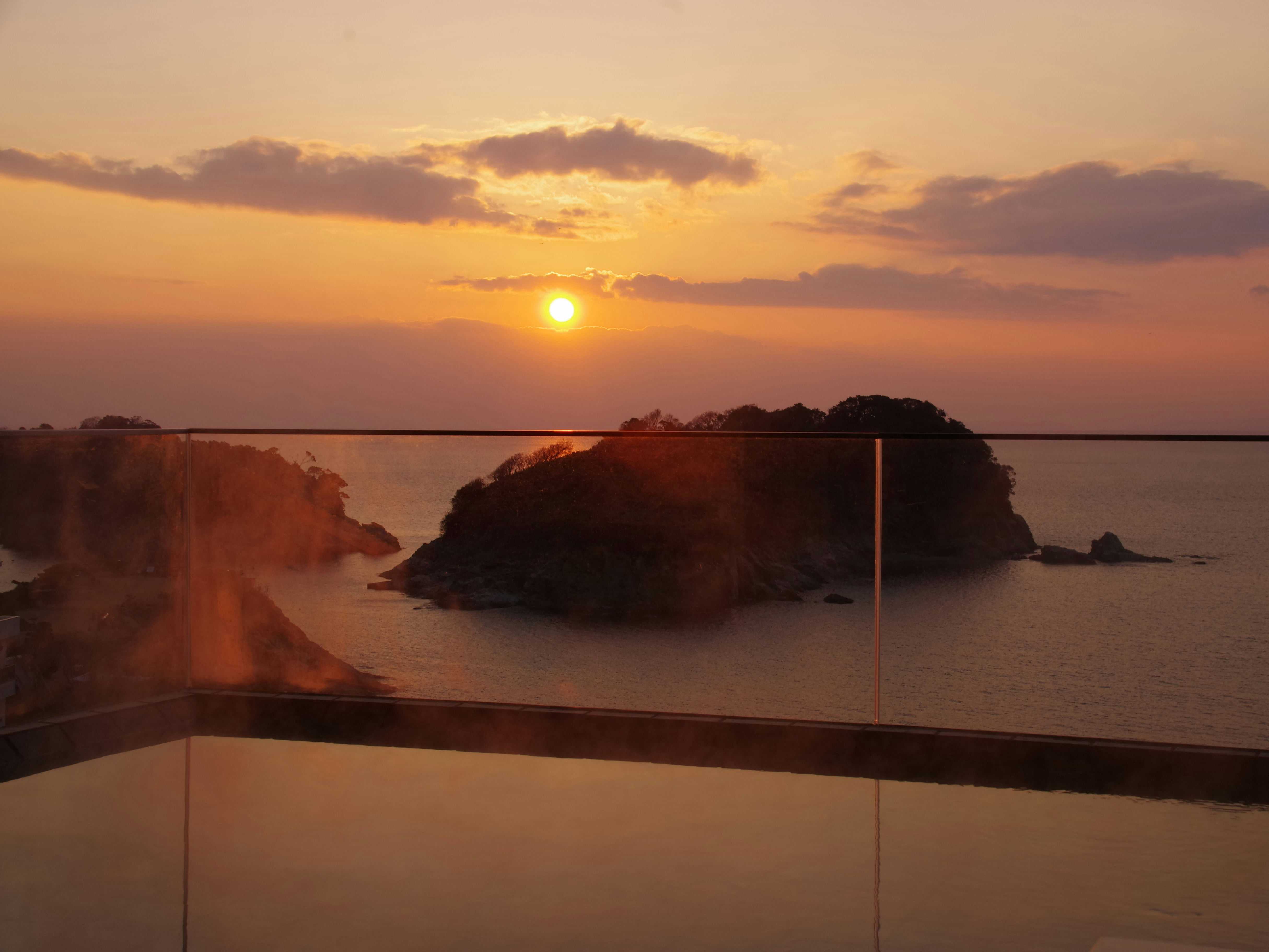 The sun setting beyond dark islands across the sea.