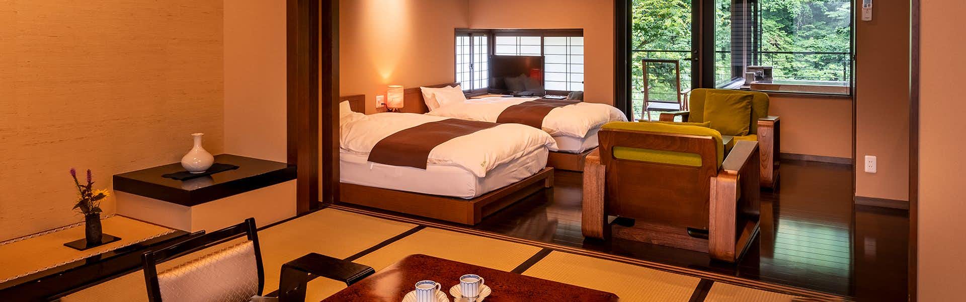 Shinshu Yamada Onsen Yamadakan Bedroom with wooden bed frame with brown horizontal stripe detail, light-colored bedding, wooden nightstand, window with natural light.