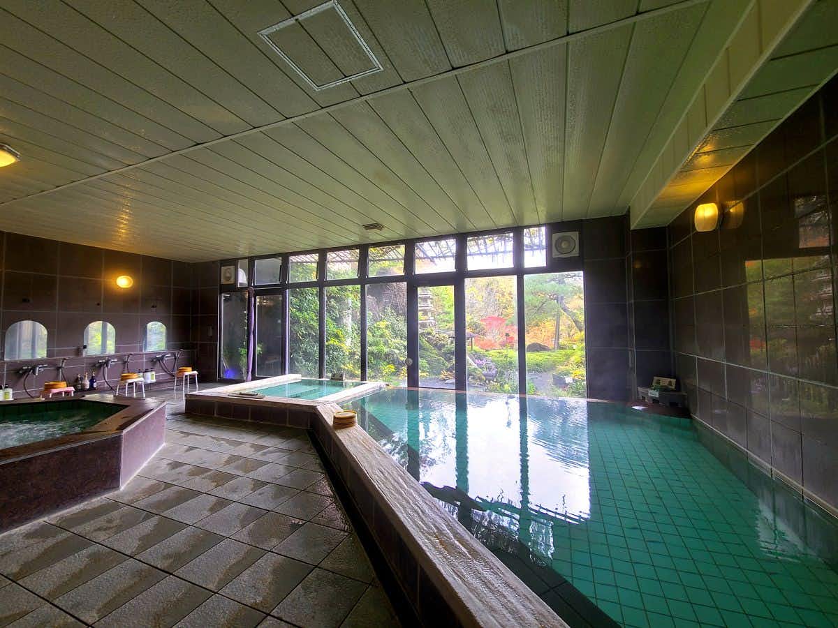 Shinkashi Onsen Gohousou with a broad indoor bath reflecting tall mountain-facing windows.