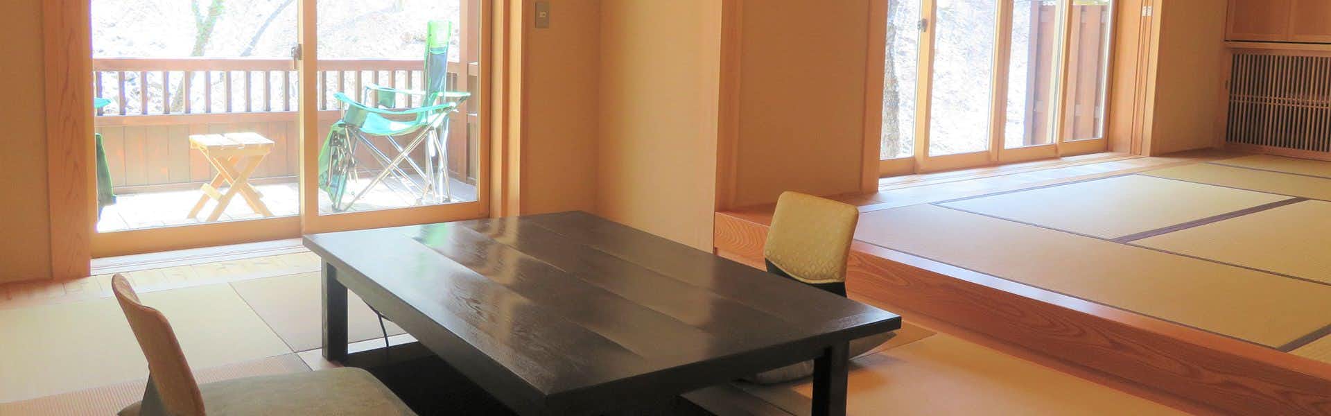 Shiriyaki Onsen Hoshigaoka Sanso Light wood walls, dark table, wooden chair with light-colored seat, wooden-framed windows, natural daylight.