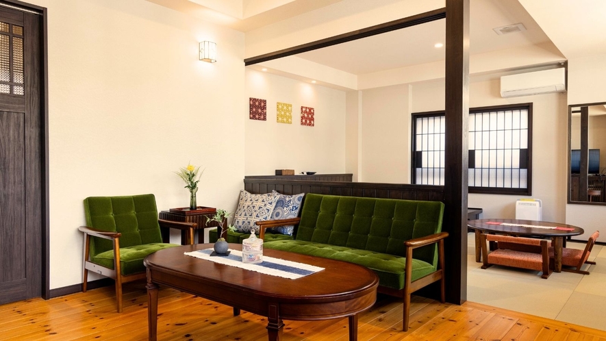 Green upholstered seating and wooden tables in a guest-room sitting area.