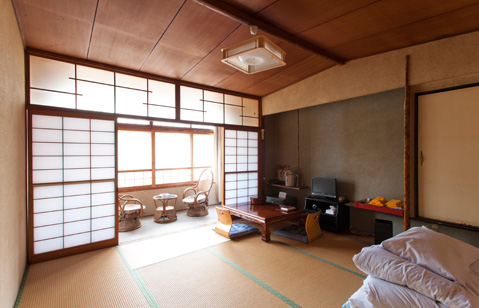 Tatami guest room with futon bedding, a low table and window-side chairs.