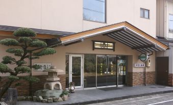 The ryokan entrance beneath a tiled gable beside a clipped tree.
