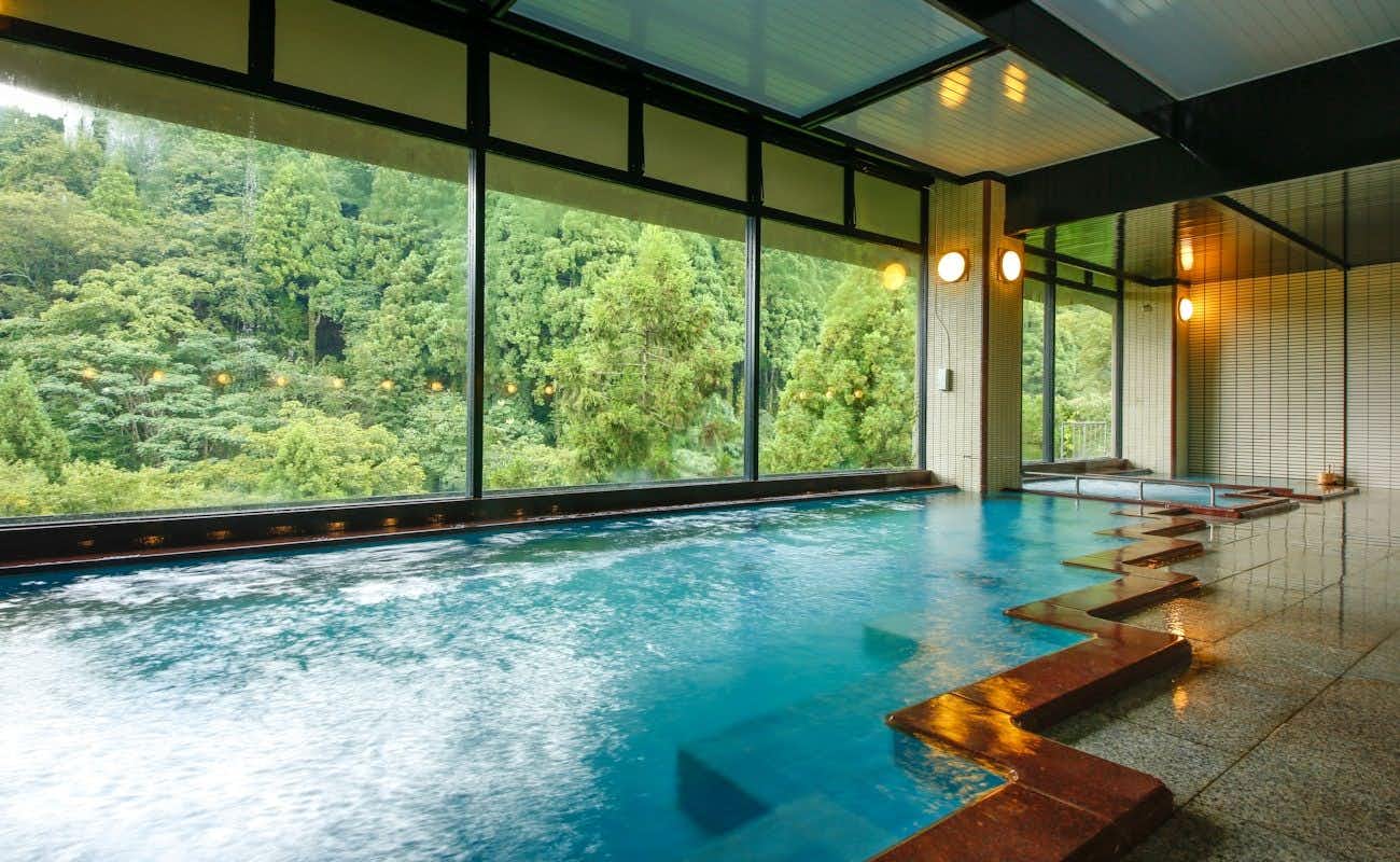 Yamanaka Onsen Yubatake no Yado Hanatsubaki with a broad indoor mineral bath overlooking forested hills.