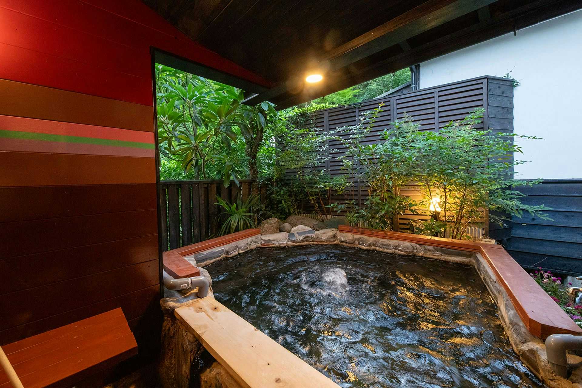 Yufuin Onsen Villa Konjakuan with this scene, where a square stone bath bubbles beside red walls and a screened garden.