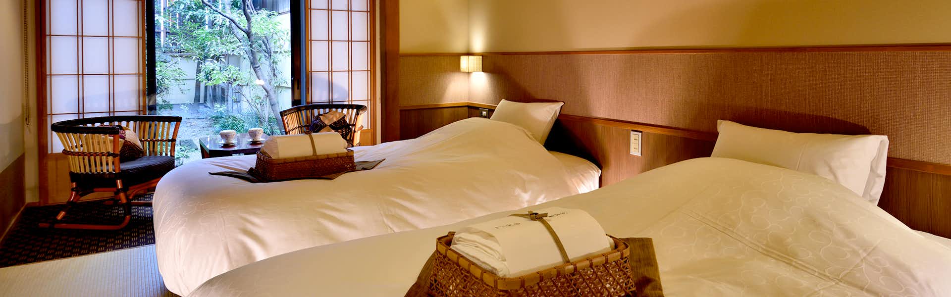 Kyokoyado Yutone Interior with white bedding, wood-paneled walls, window seating area with cushions, and garden view framed by wooden furnishings.