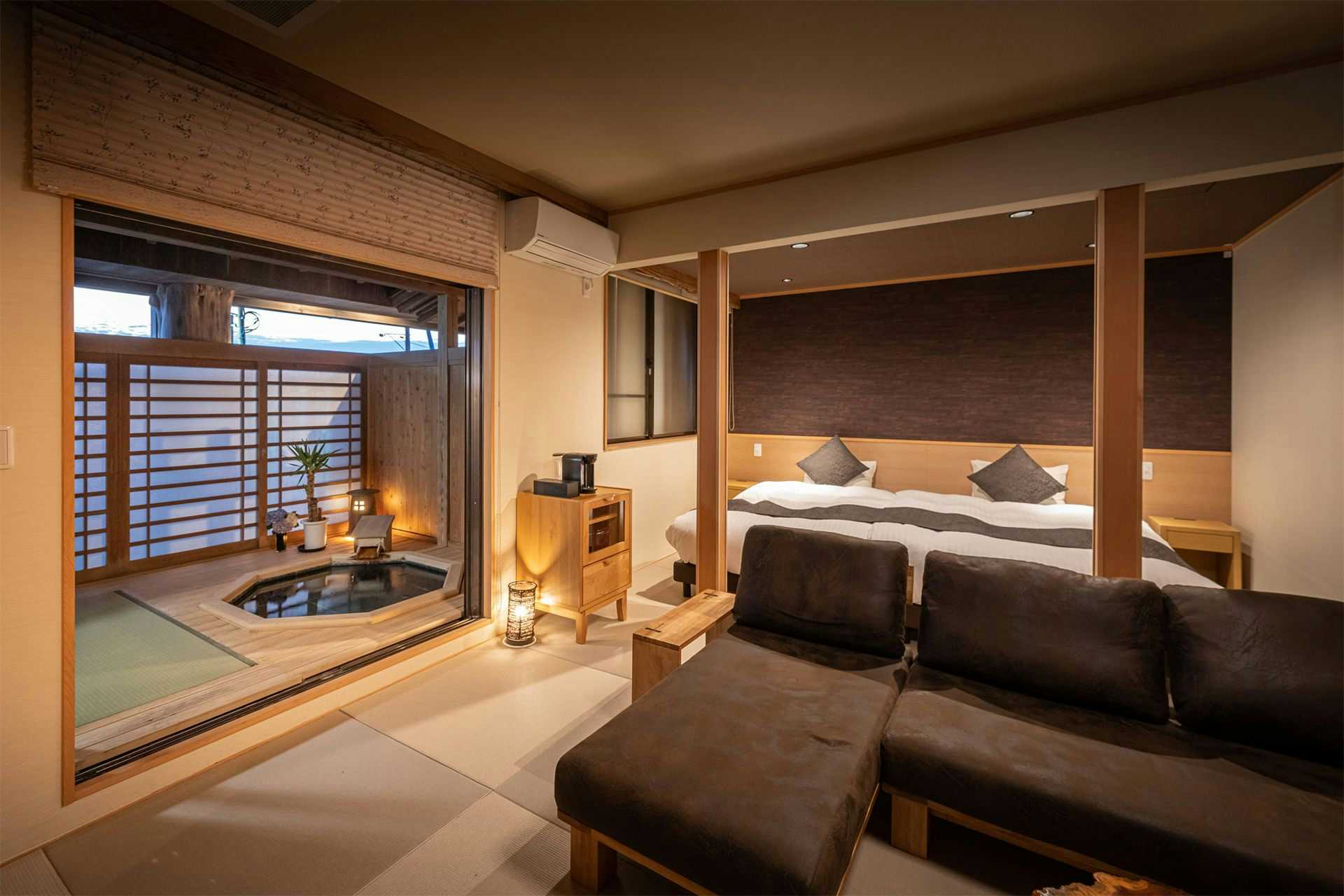 Kappo Ryokan Kiyoto room with twin beds, a dark sofa and a square bath beyond glass doors