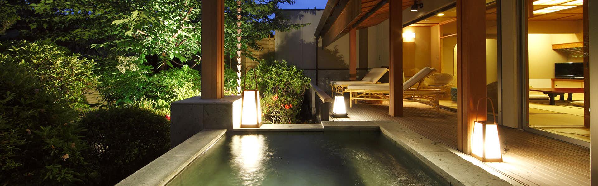 Yumeguri no Yado Yoshiharu rectangular bath with clear water, wood building with floor-to-ceiling windows and warm interior lighting, forest surrounding