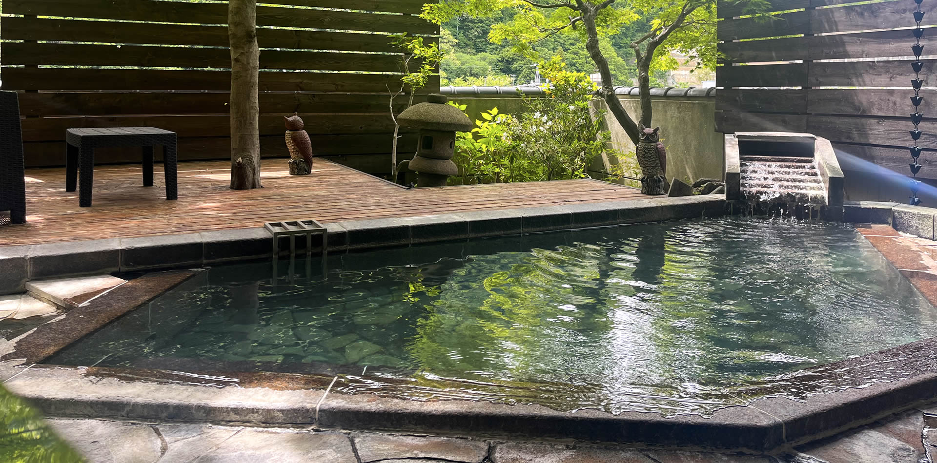 Outdoor bathing pool with a wooden deck, stone lanterns, and a water feature.