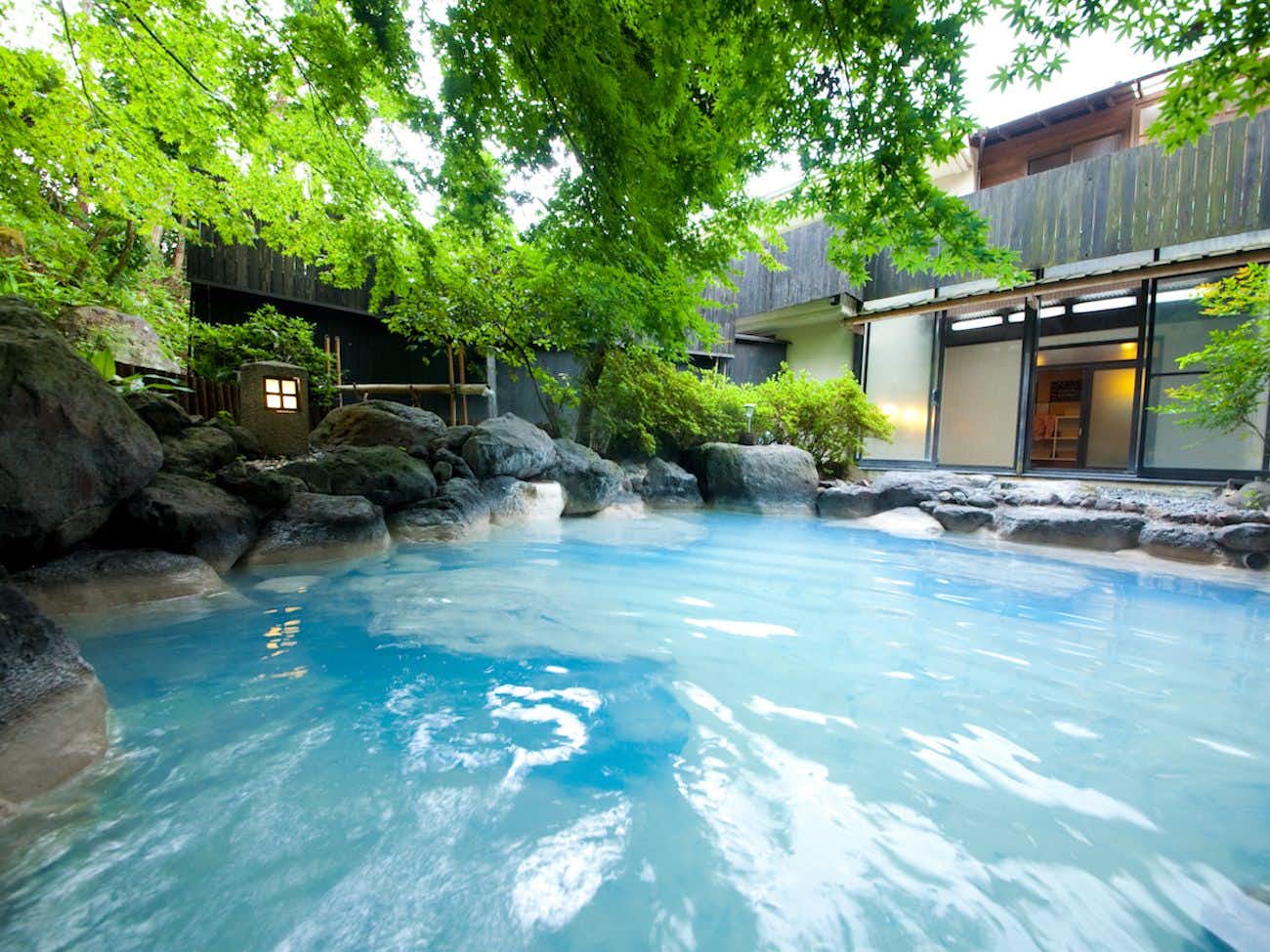 Yufuin Taiha with a milky blue outdoor bath surrounded by rocks and green trees.